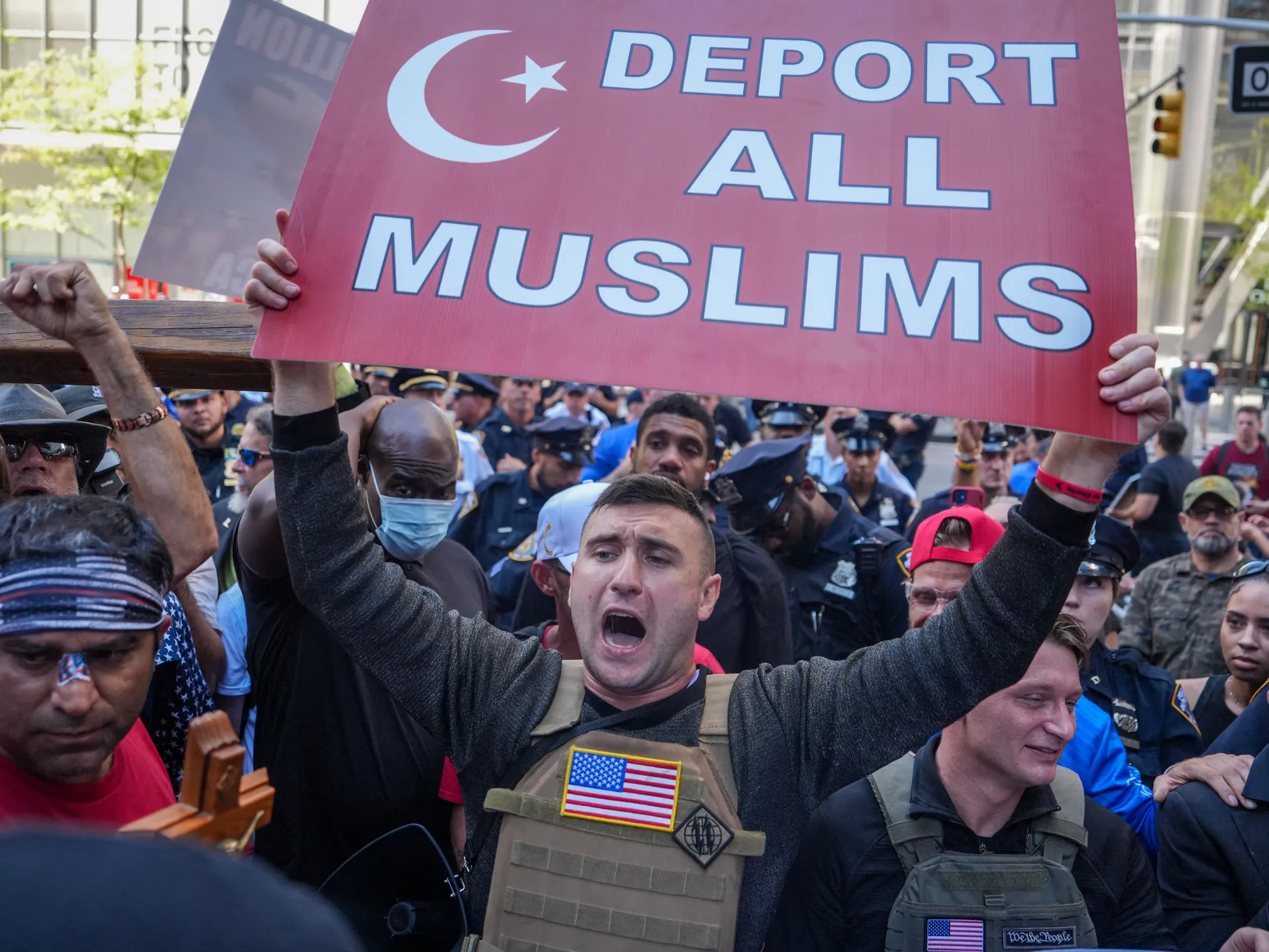 Crowd member raises a sign reading “Deport All Muslims” during a tense street demonstration.