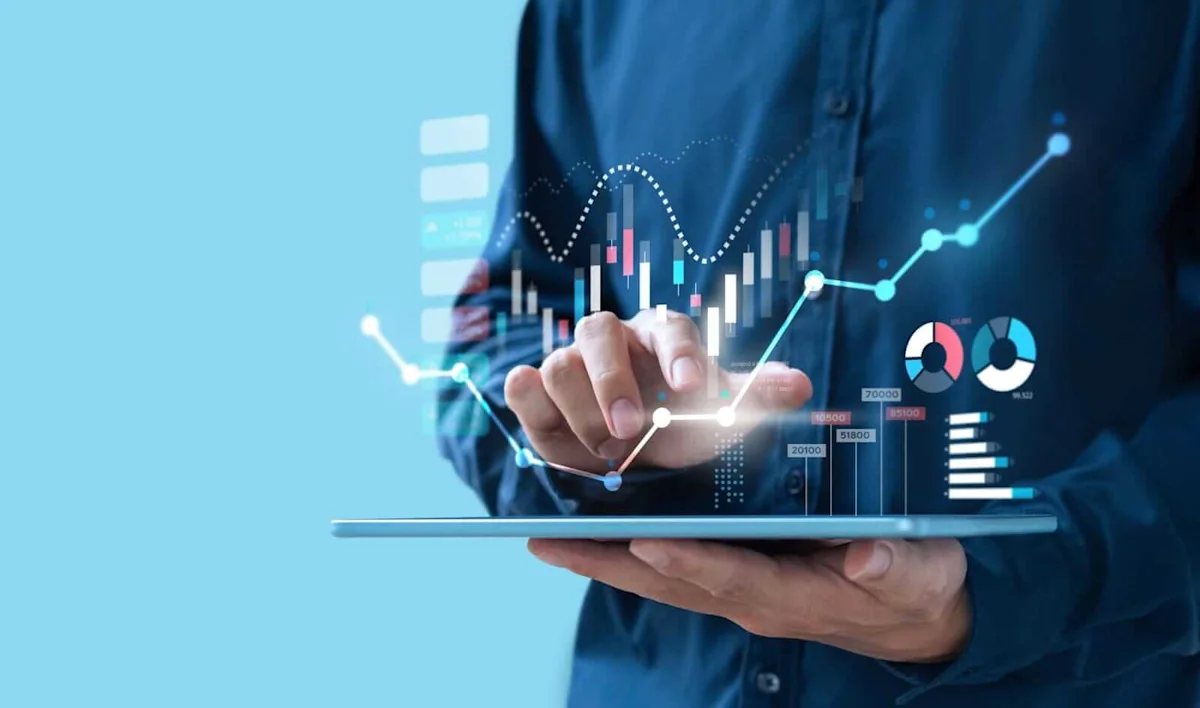 Businessperson holding a tablet displaying colorful financial charts, graphs, and upward-trending market data.