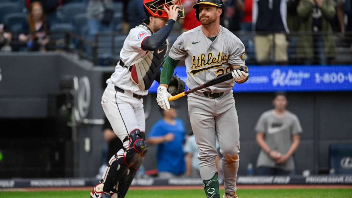 An Athletics batter walks past a catcher holding his mask in a baseball stadium.