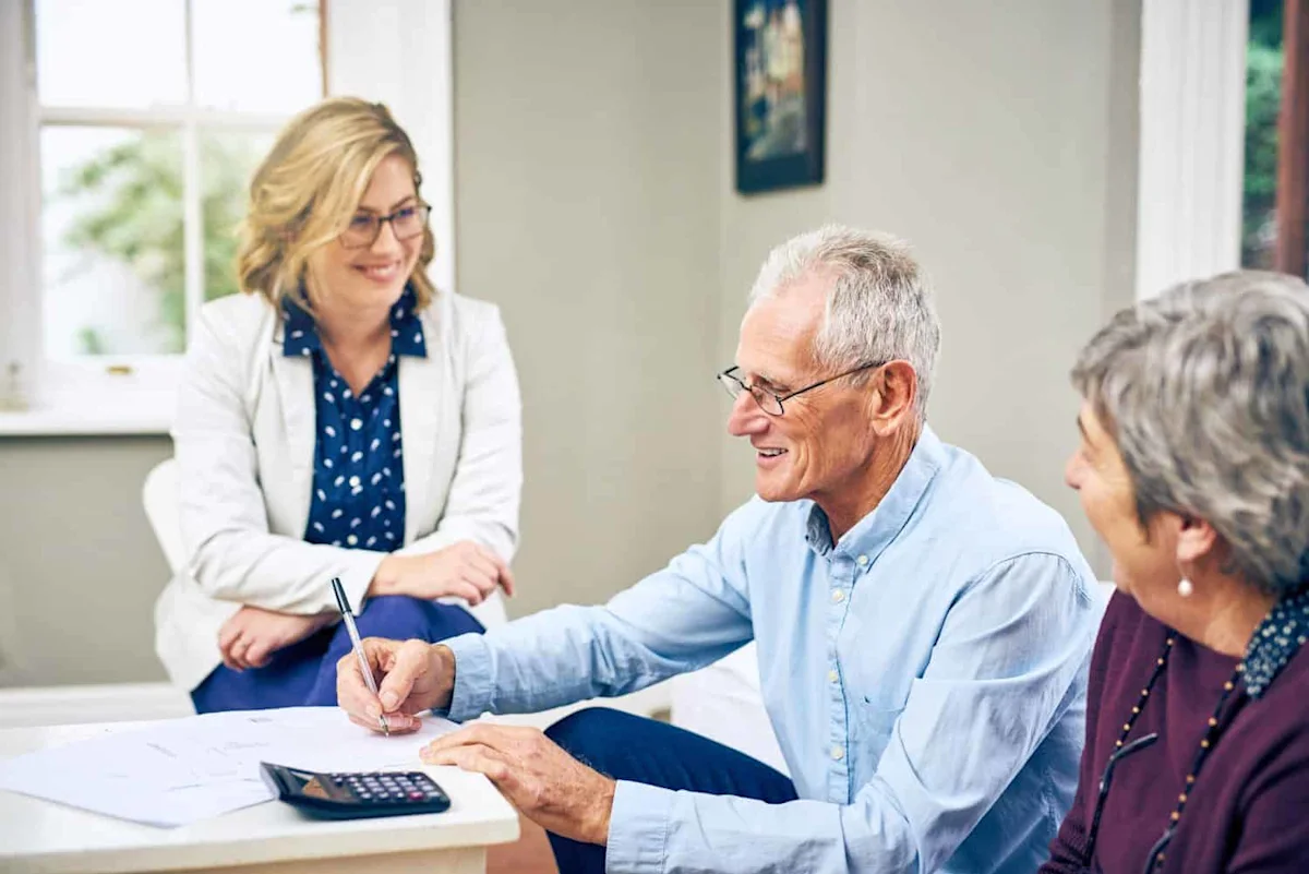 Older couple review paperwork with a financial adviser at a table.