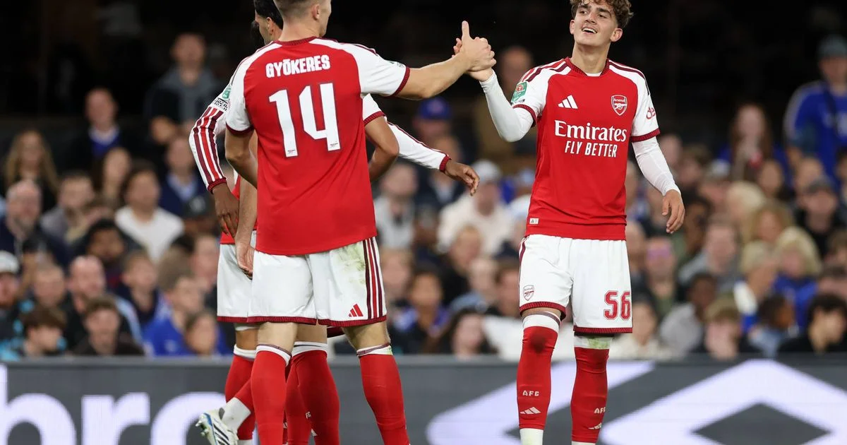 Arsenal players celebrate together during a football match, with shirts numbered 14 and 56 visible.