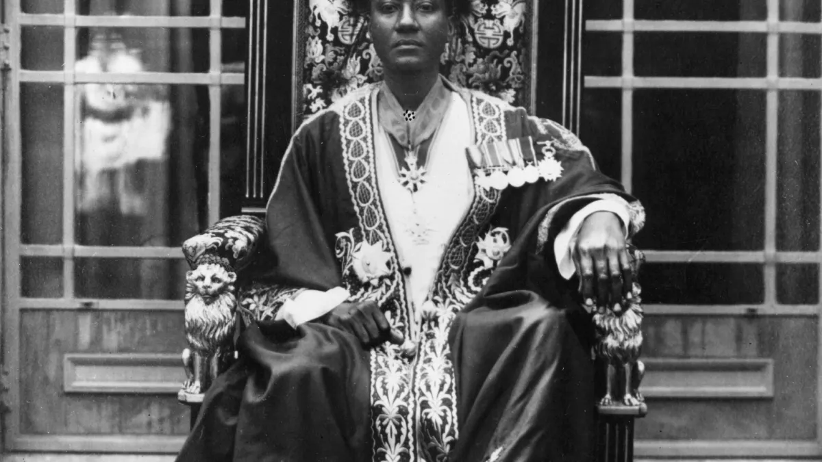 Black-and-white portrait of a formally dressed woman seated on an ornate throne-like chair.