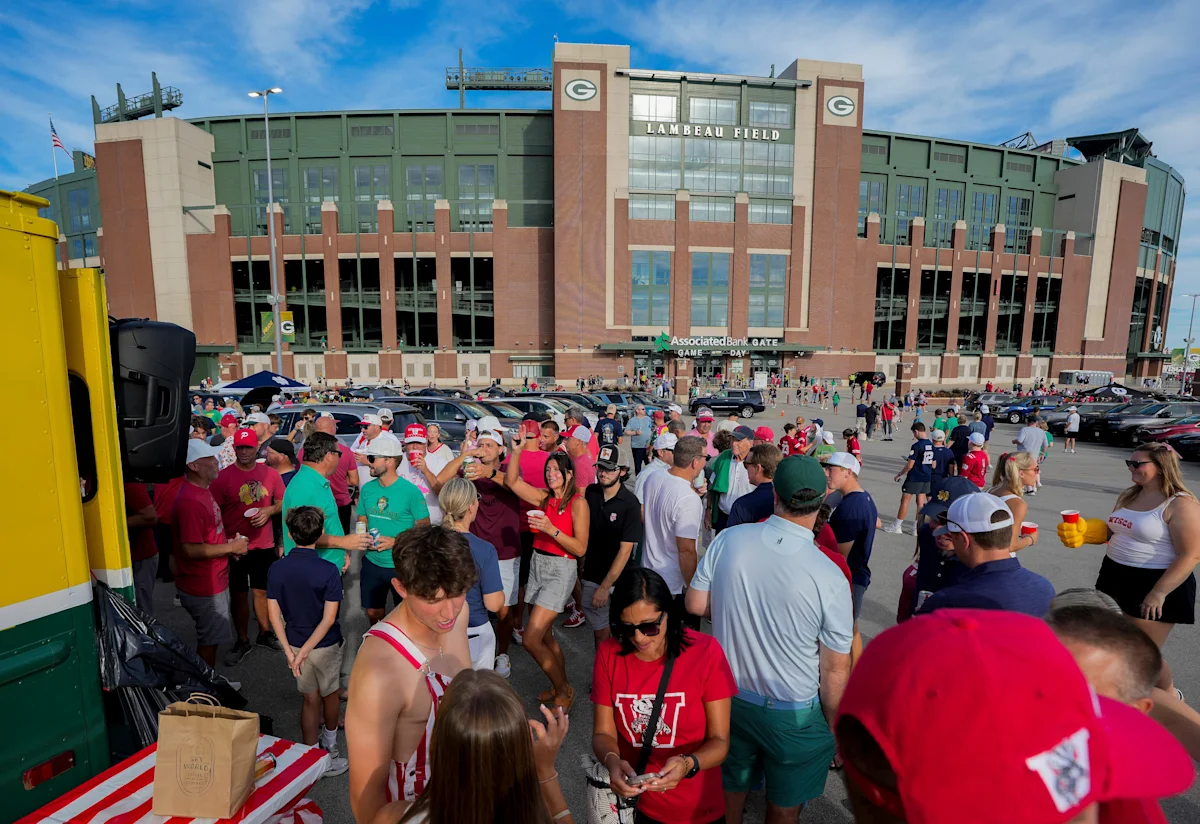 Fans gather in a parking lot outside Lambeau Field as crowds fill the foreground.