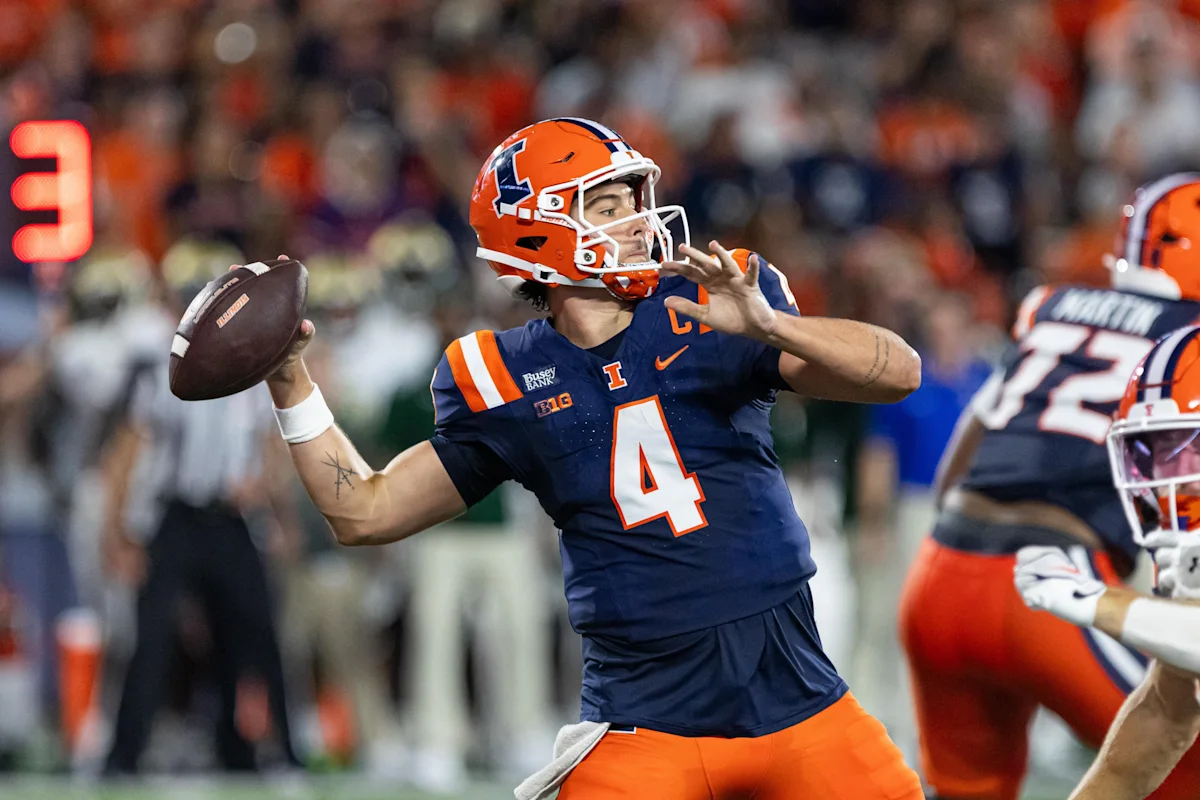 Illinois quarterback in orange helmet and navy jersey prepares to throw a football during a game