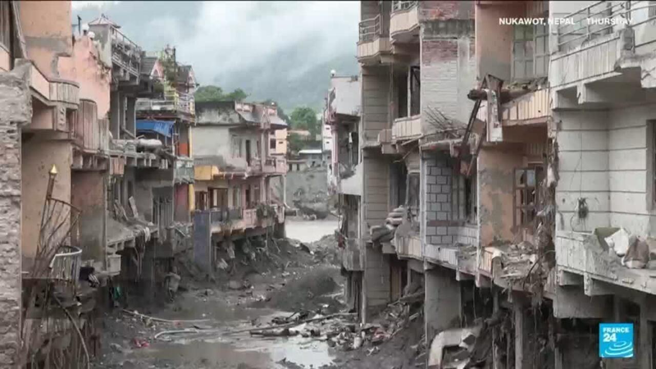 Flood debris and muddy water fill a narrow street between damaged, partially collapsed buildings.