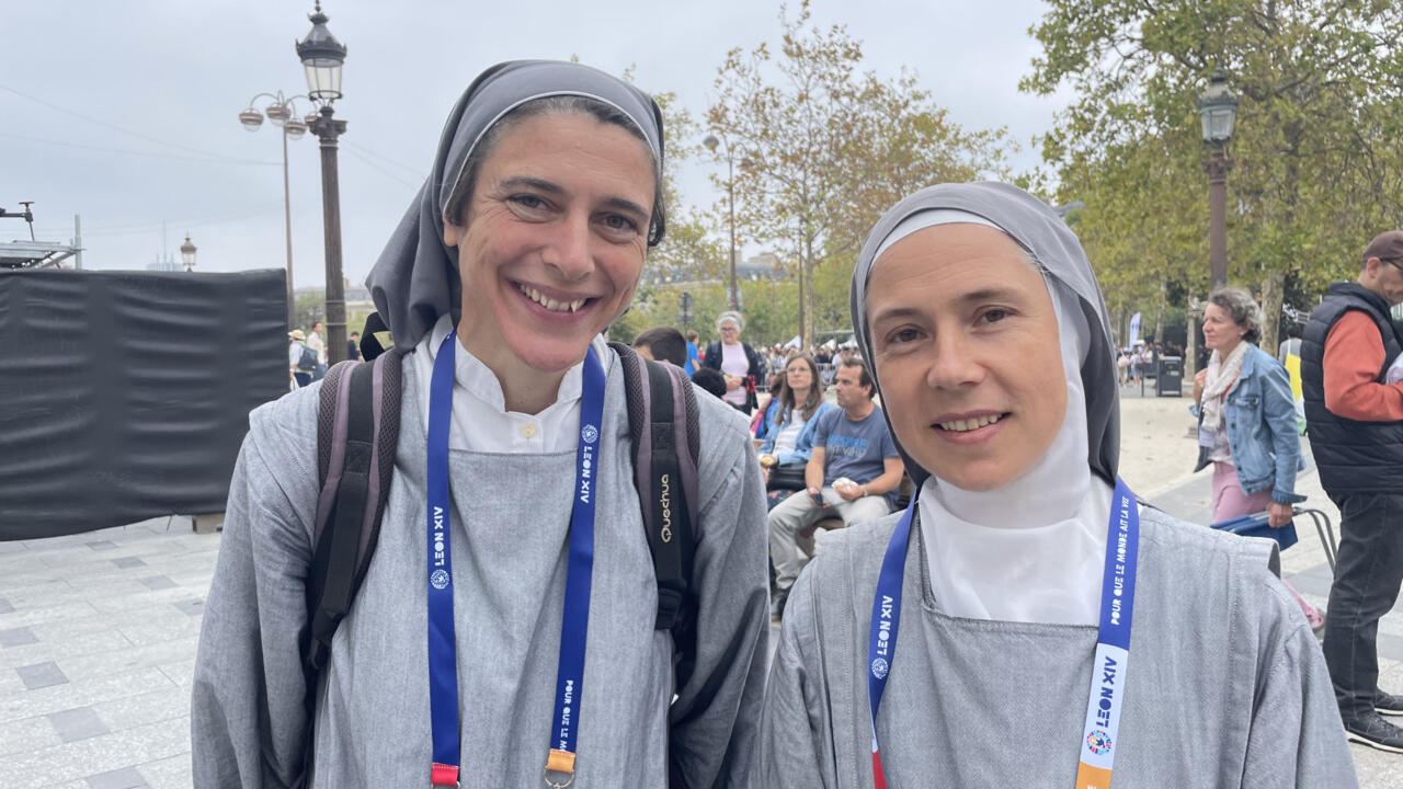Two people wearing gray religious habits and blue event lanyards smile at an outdoor gathering.