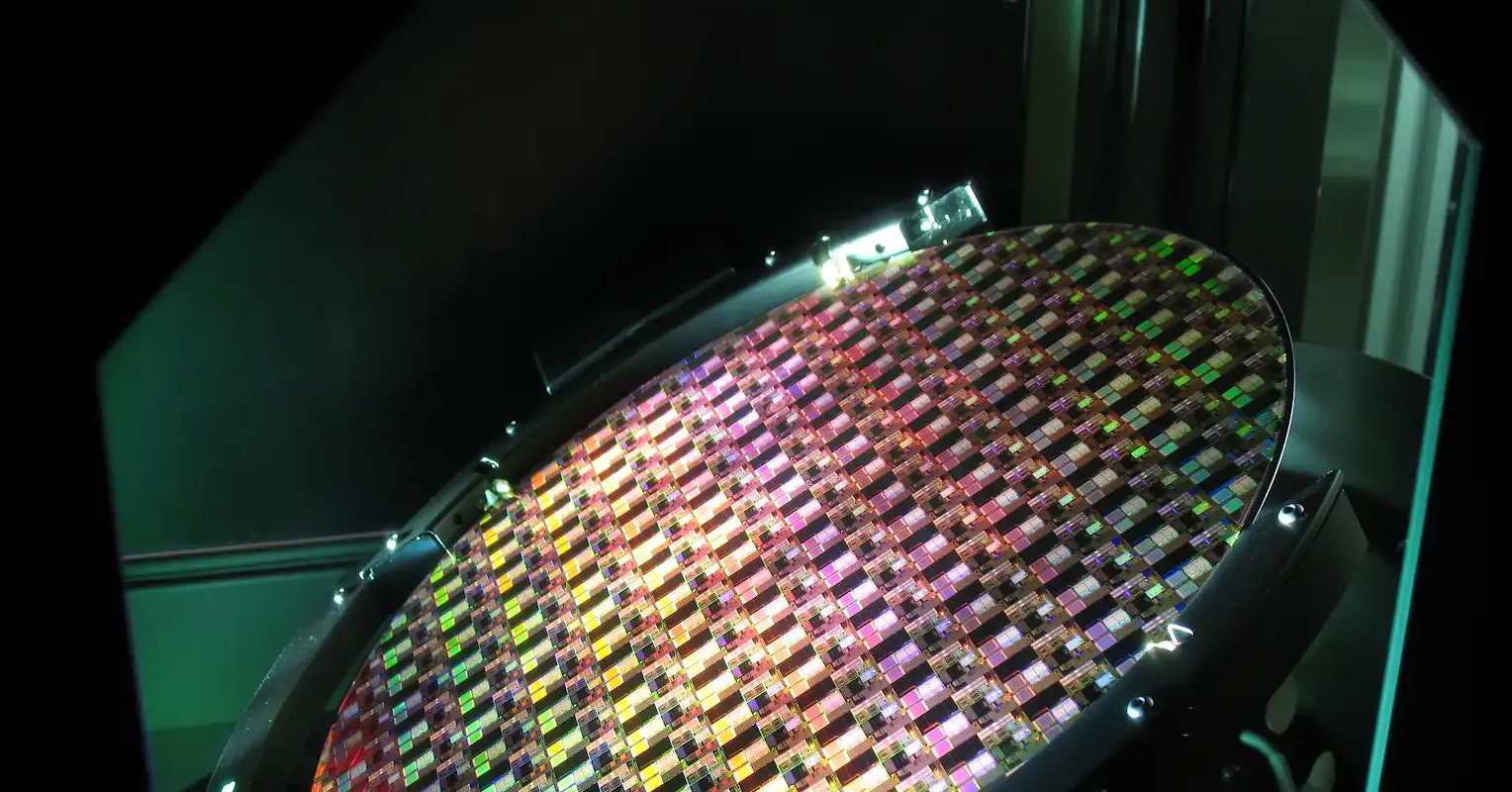 Close-up of a colorful semiconductor wafer inside illuminated laboratory equipment.