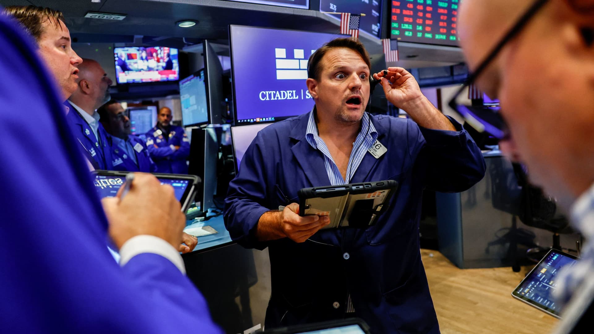 Traders work among electronic market screens on a busy exchange floor.