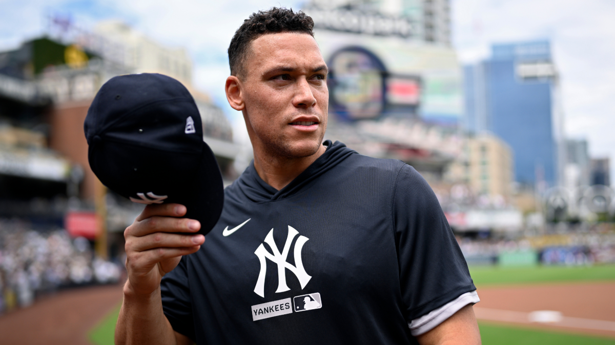 Baseball player in Yankees shirt holds a black cap near the field during warmups.