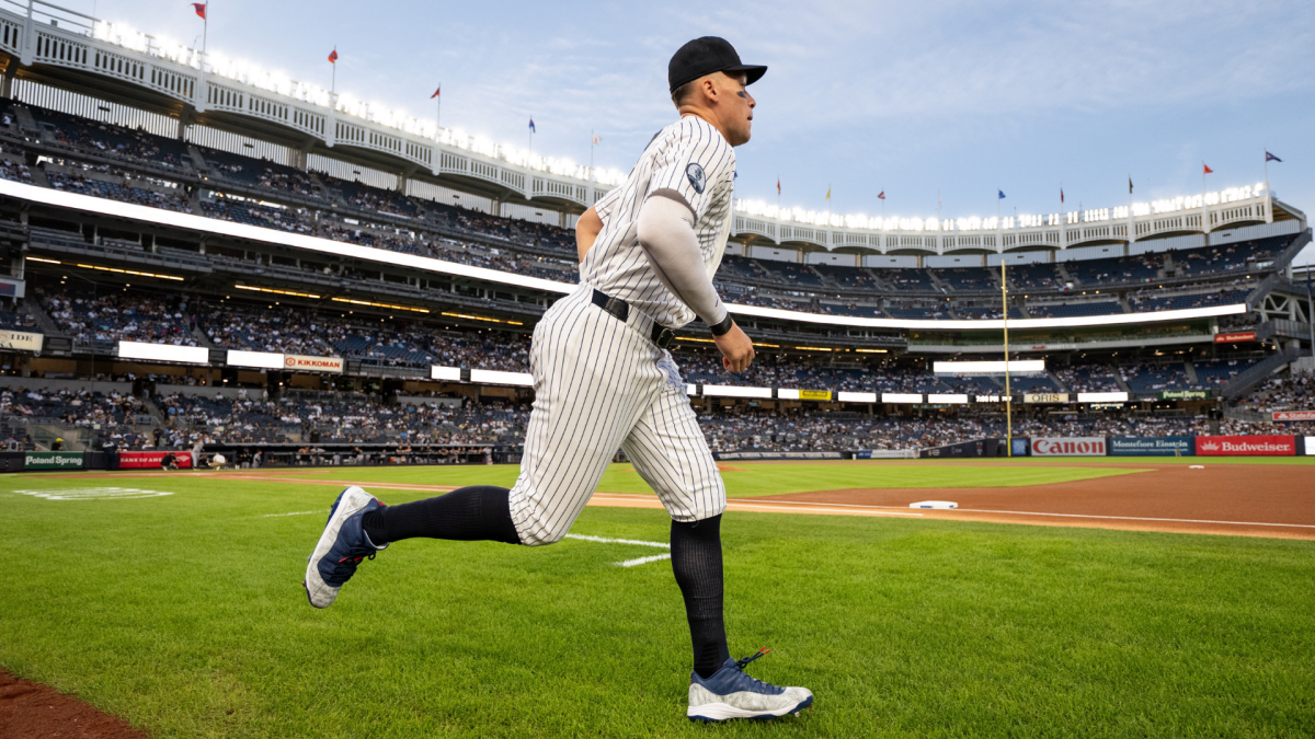 A Yankees player runs across the grass at a baseball stadium during a game.