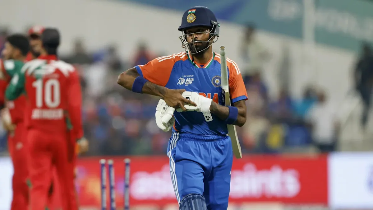 A cricketer in blue and orange kit holds a bat while wearing a helmet and pads.