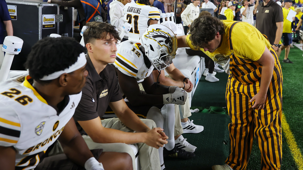 Western Michigan players and staff confer on the sideline as a costumed fan stands nearby.