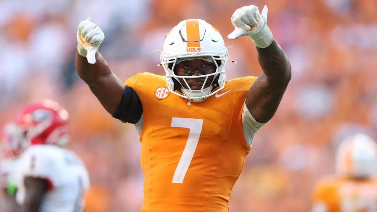 Football player in orange jersey and helmet raises both fists during a game.