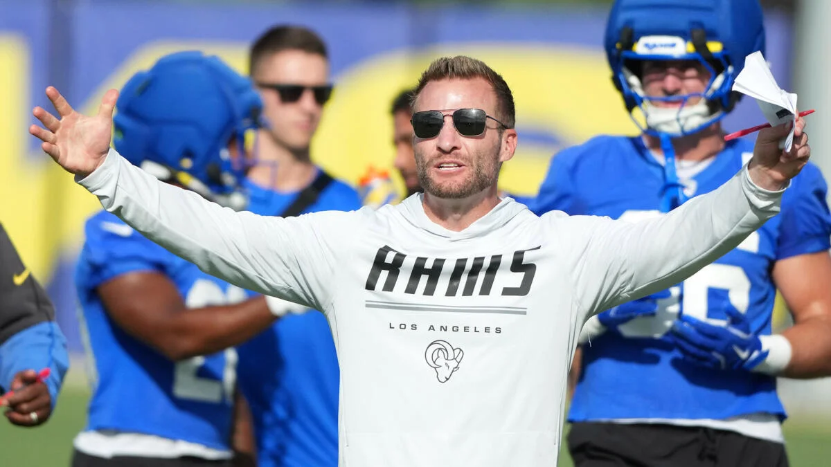A man in sunglasses spreads his arms during a Rams football practice.