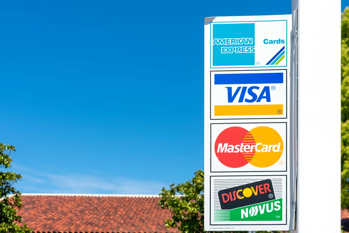 Outdoor sign displays American Express, Visa, Mastercard and Discover card logos against blue sky.