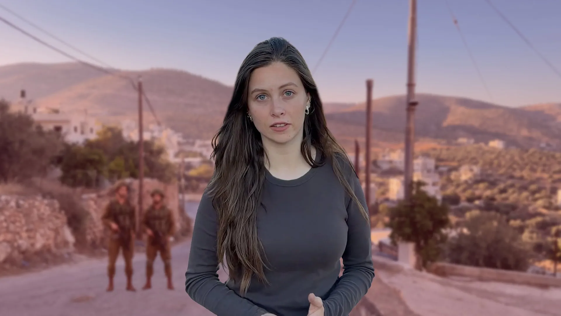Woman standing on a village road with hills, utility poles, and two blurred figures behind her.