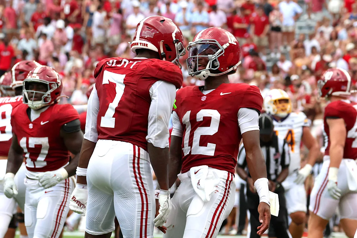 Alabama football players in crimson uniforms gather on the field during a game.