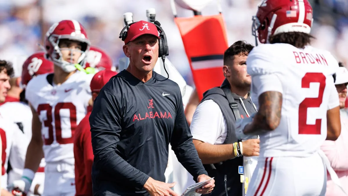Alabama coach in headset stands among players during a college football game