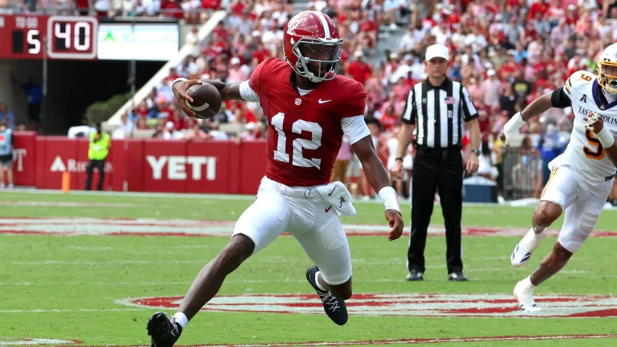 Alabama quarterback in crimson jersey runs with the football as Kentucky defender pursues.