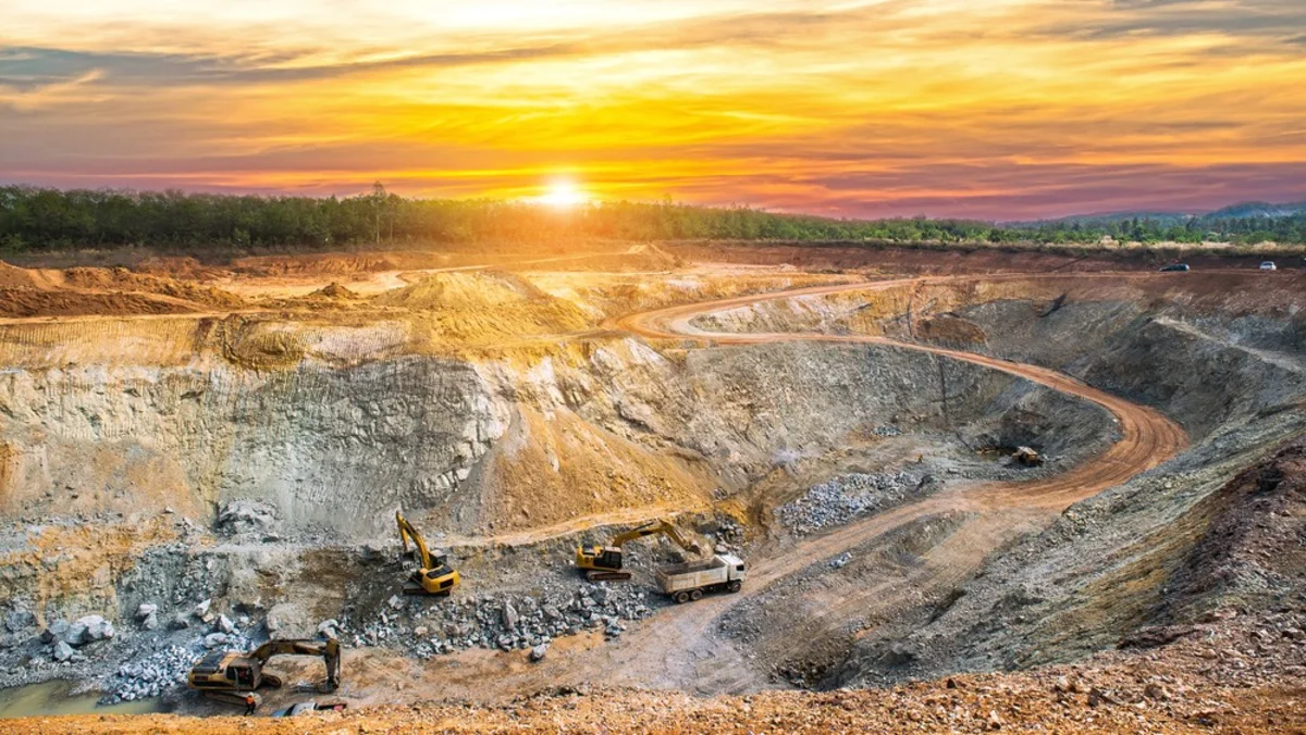 Open-pit mine with excavators and haul trucks beneath a colorful sunset