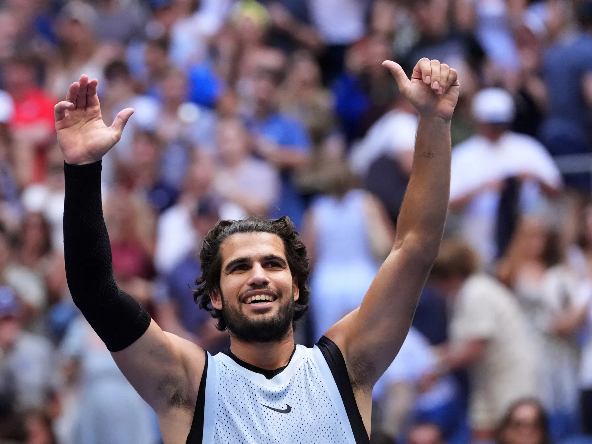 Tennis player raises both arms and smiles in celebration before a blurred crowd