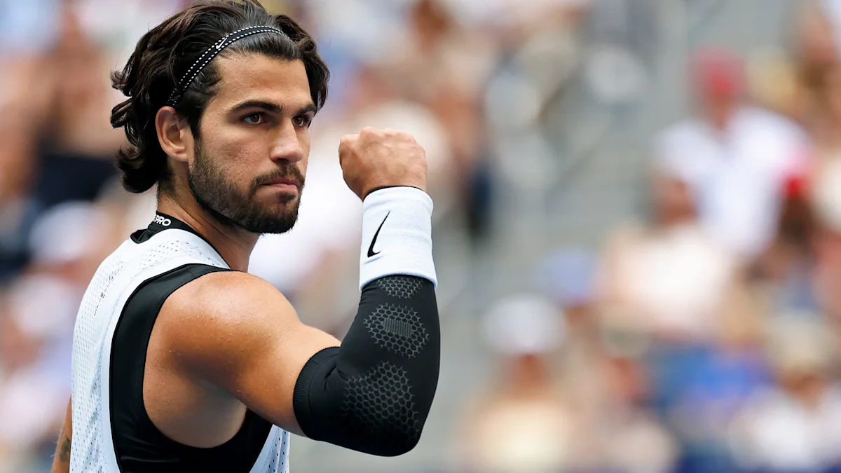 Tennis player with headband raises a clenched fist during a match