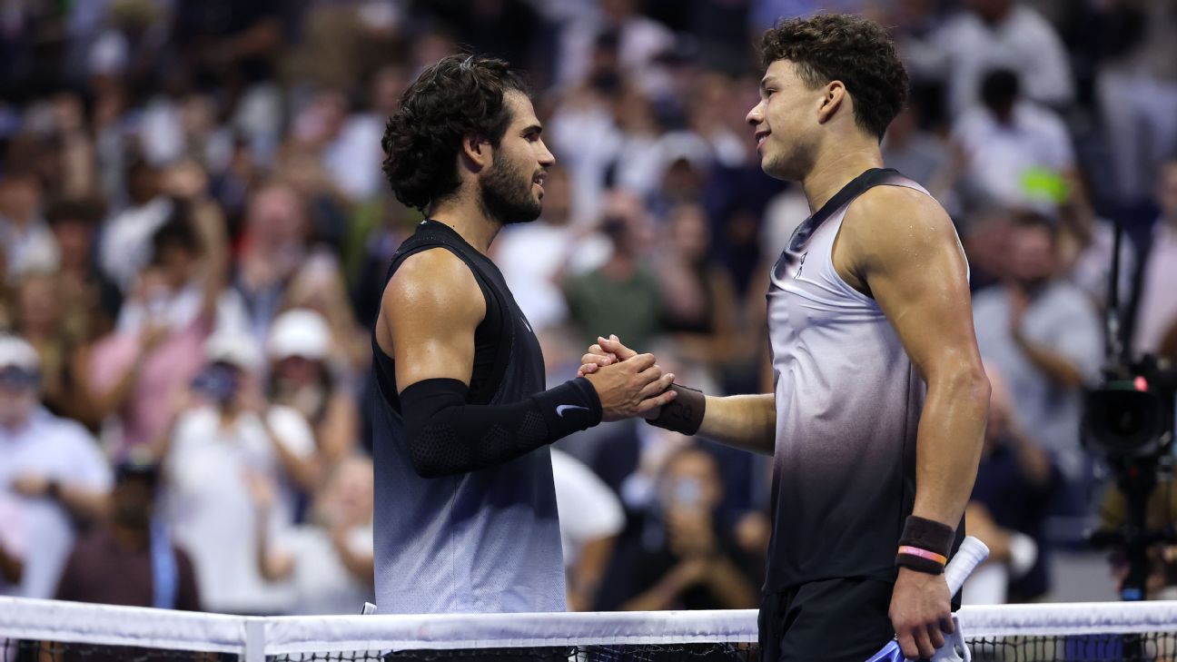 Two tennis players shake hands at the net as spectators watch from the stands