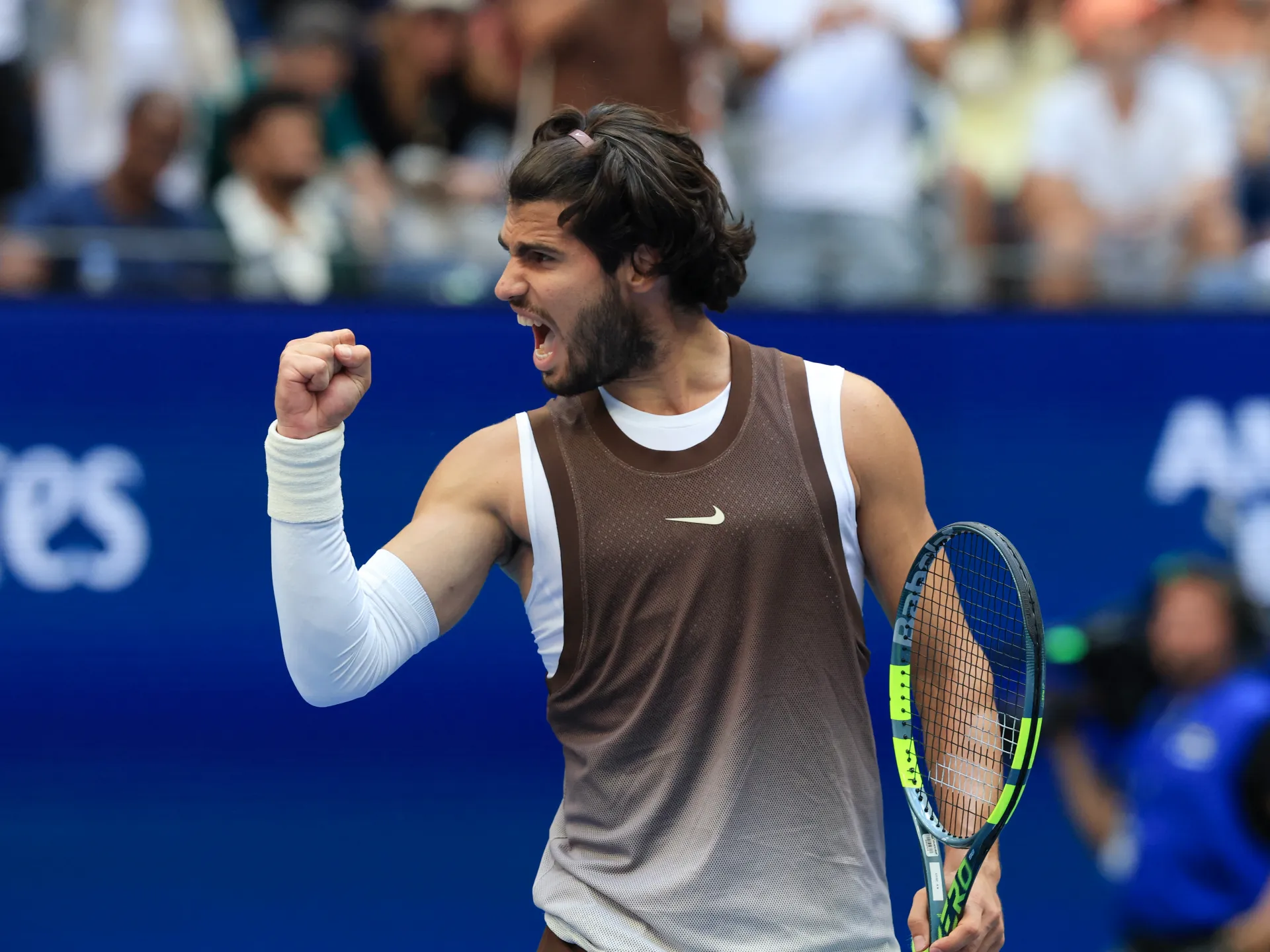 Tennis player celebrates with clenched fist while holding a racket on court.