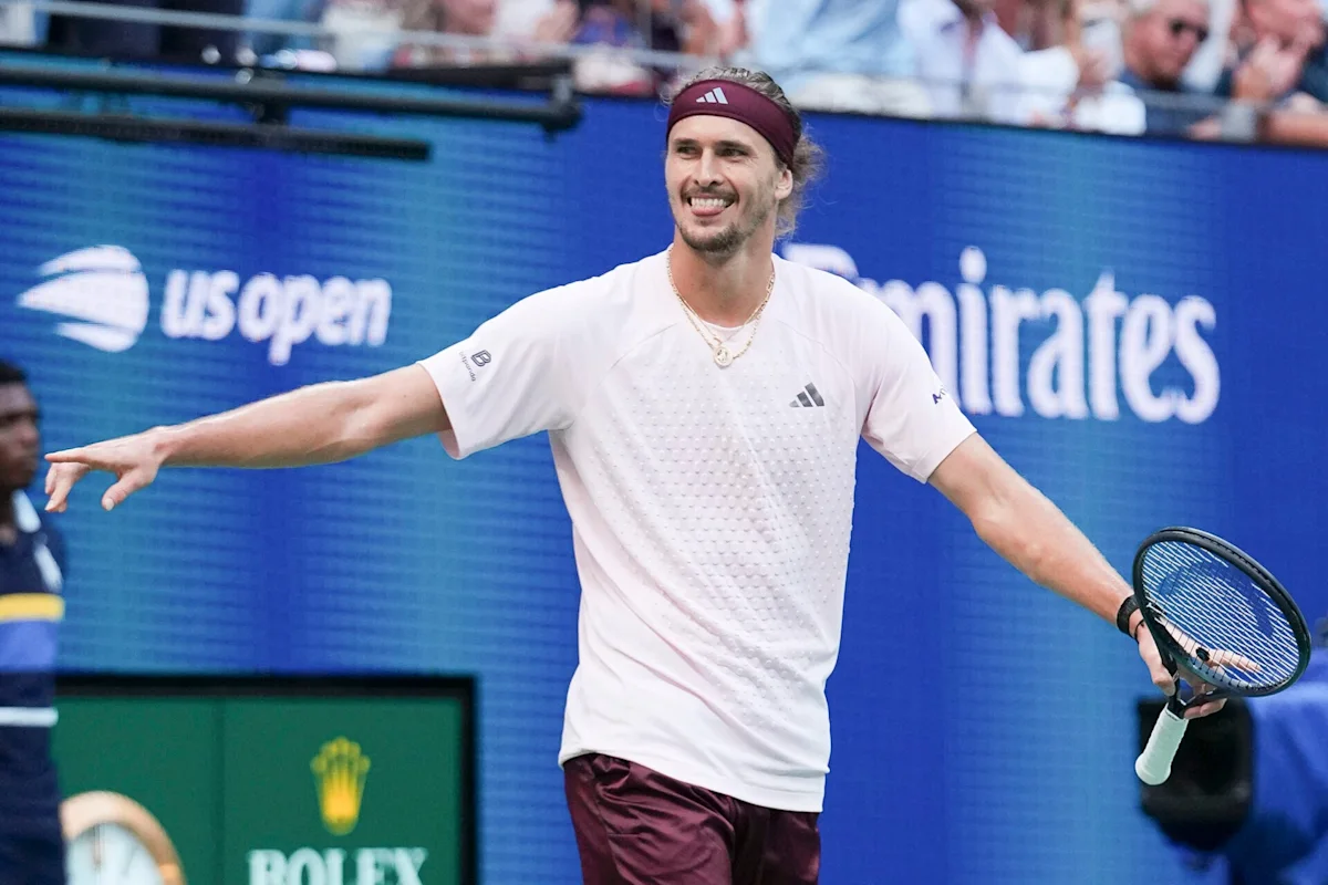 Tennis player in white shirt and burgundy shorts celebrates while holding a racket on court