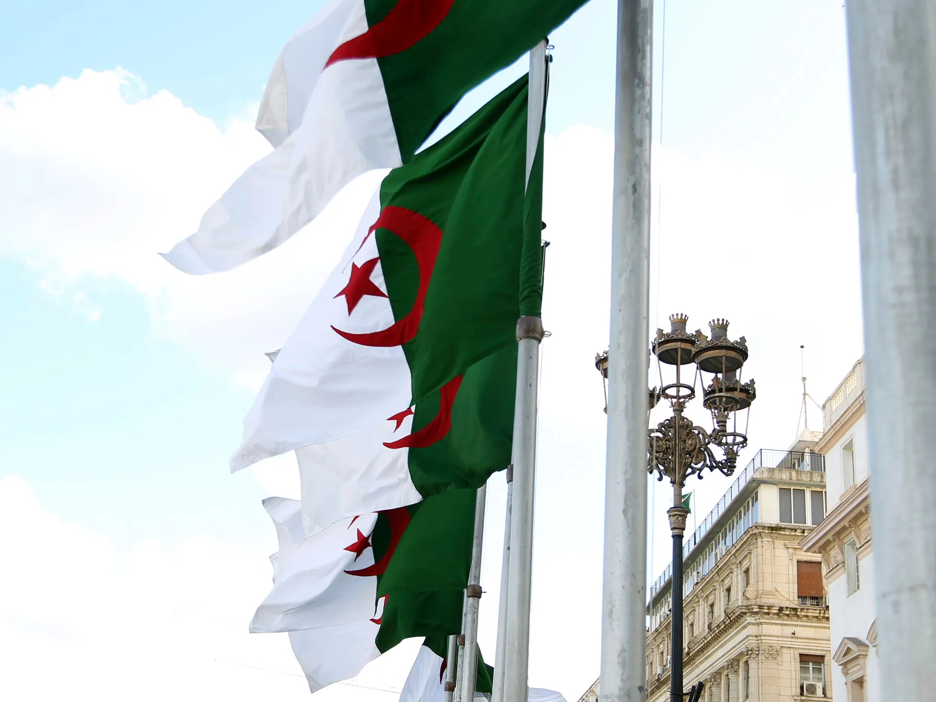 Algerian flags waving on poles beside ornate streetlights and historic urban buildings