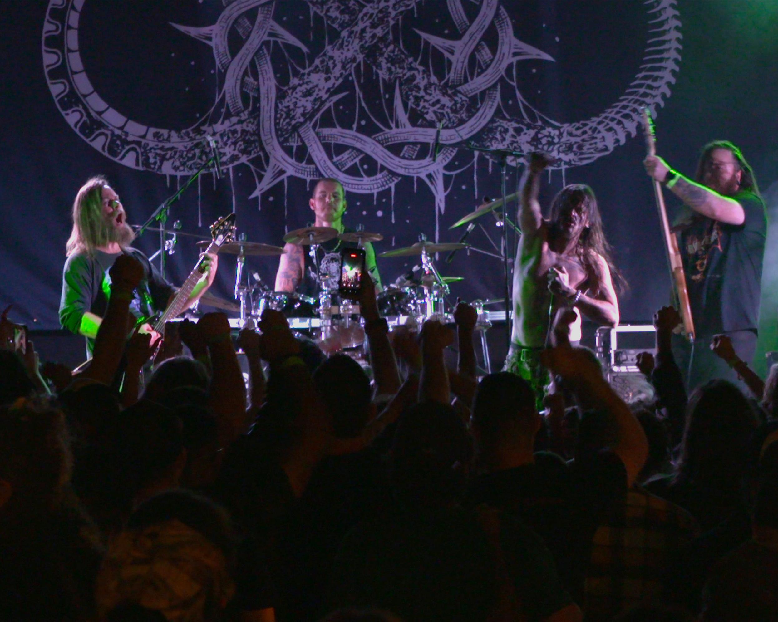 Heavy metal band performs onstage as a crowd raises hands and phones during a concert