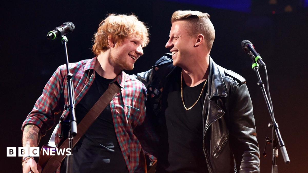 Two musicians smiling and performing together onstage beside microphones, with one holding a guitar.