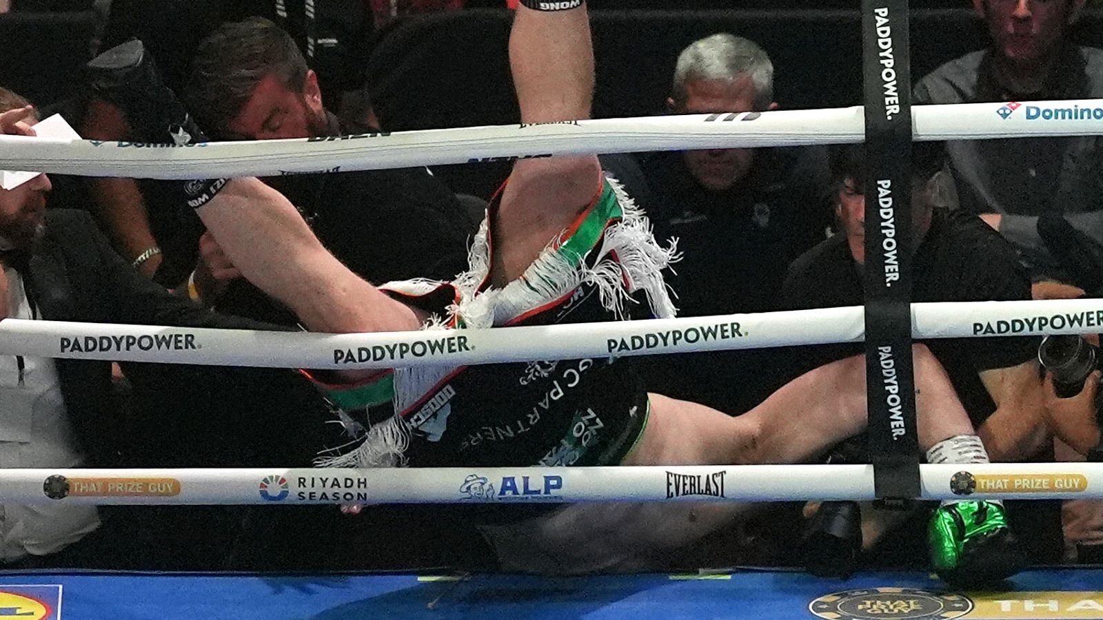 Boxer lies tangled beneath the ropes as ringside spectators and photographers look on.