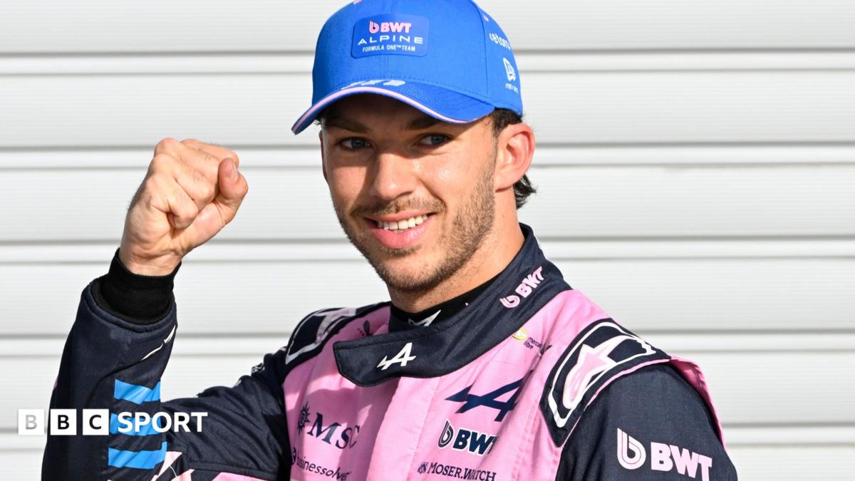 Smiling racing driver in pink Alpine suit and blue cap raises a clenched fist
