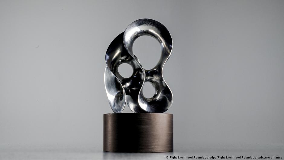 Polished abstract metal sculpture with interlocking loops displayed on a dark cylindrical pedestal.