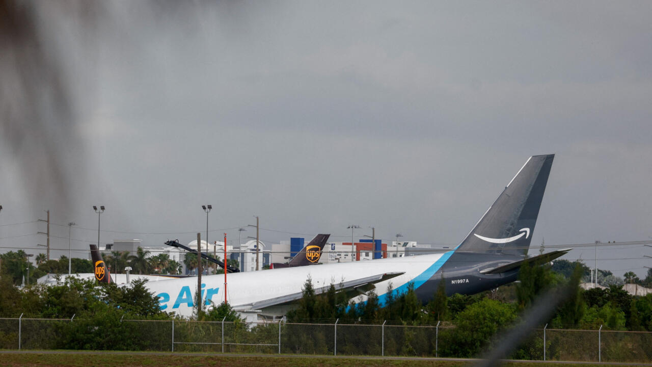Amazon cargo plane behind an airport perimeter fence under an overcast sky