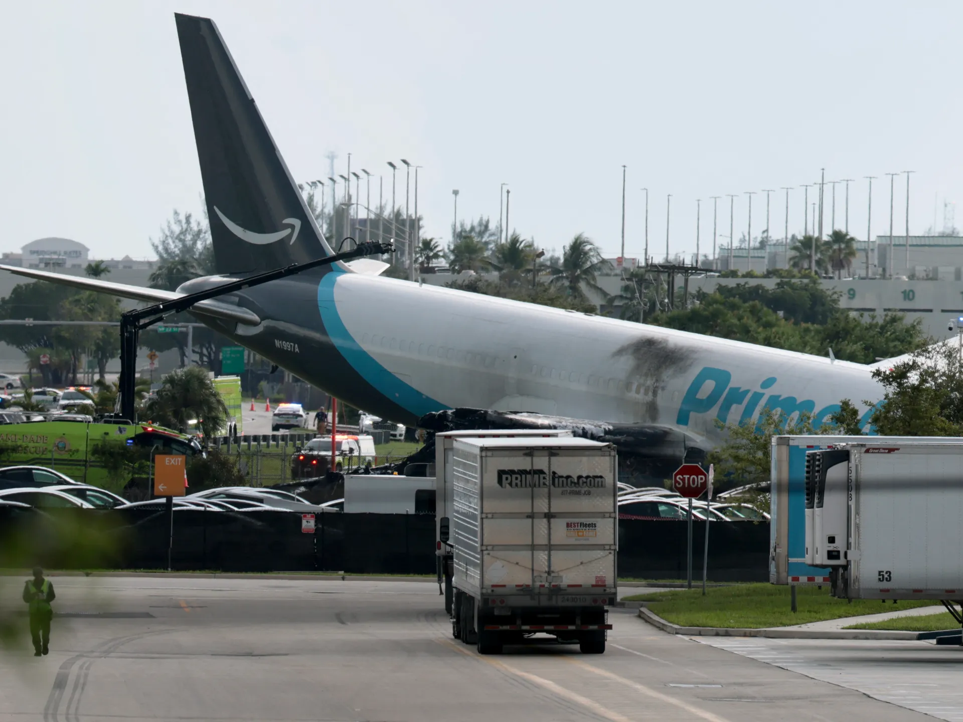 Amazon Prime Air cargo plane damaged near airport roadway with emergency vehicles and trucks nearby