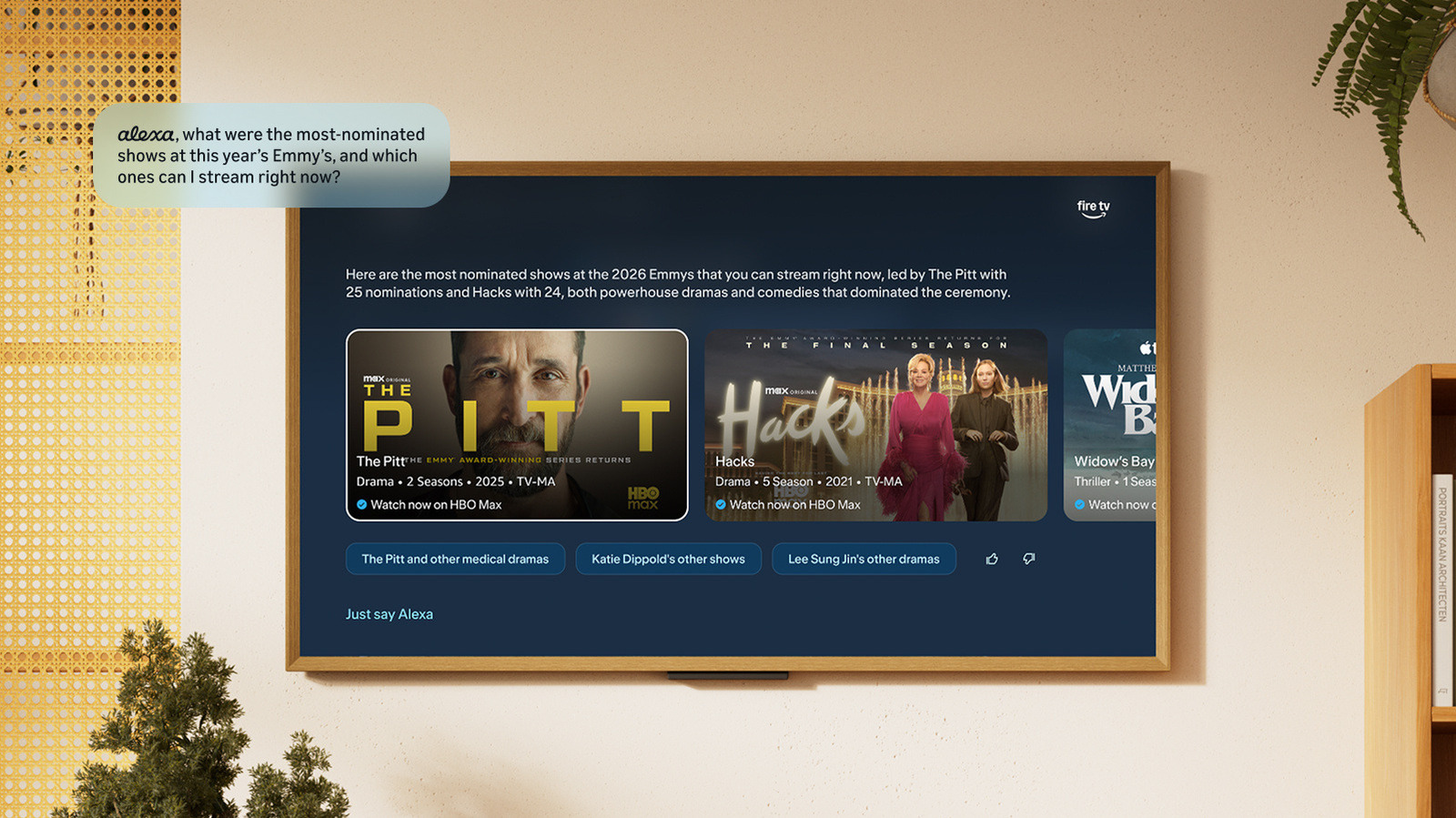 A wall-mounted Fire TV displays Emmy show recommendations beneath an Alexa question bubble in a living room.