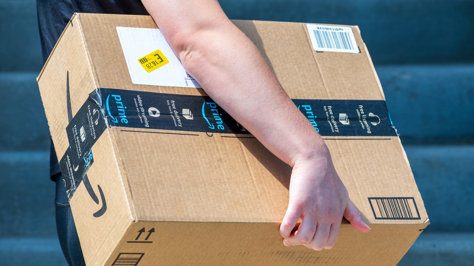 Person carrying a large Amazon Prime cardboard package outdoors