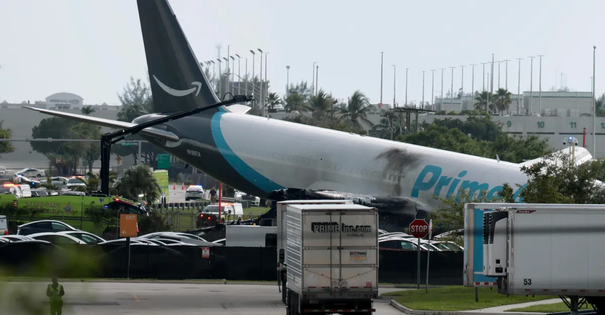 Damaged Amazon Prime cargo plane fuselage rests near airport roads and emergency vehicles.