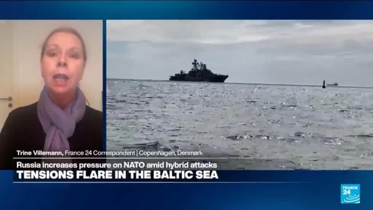 News broadcast showing a woman correspondent beside a naval vessel at sea.