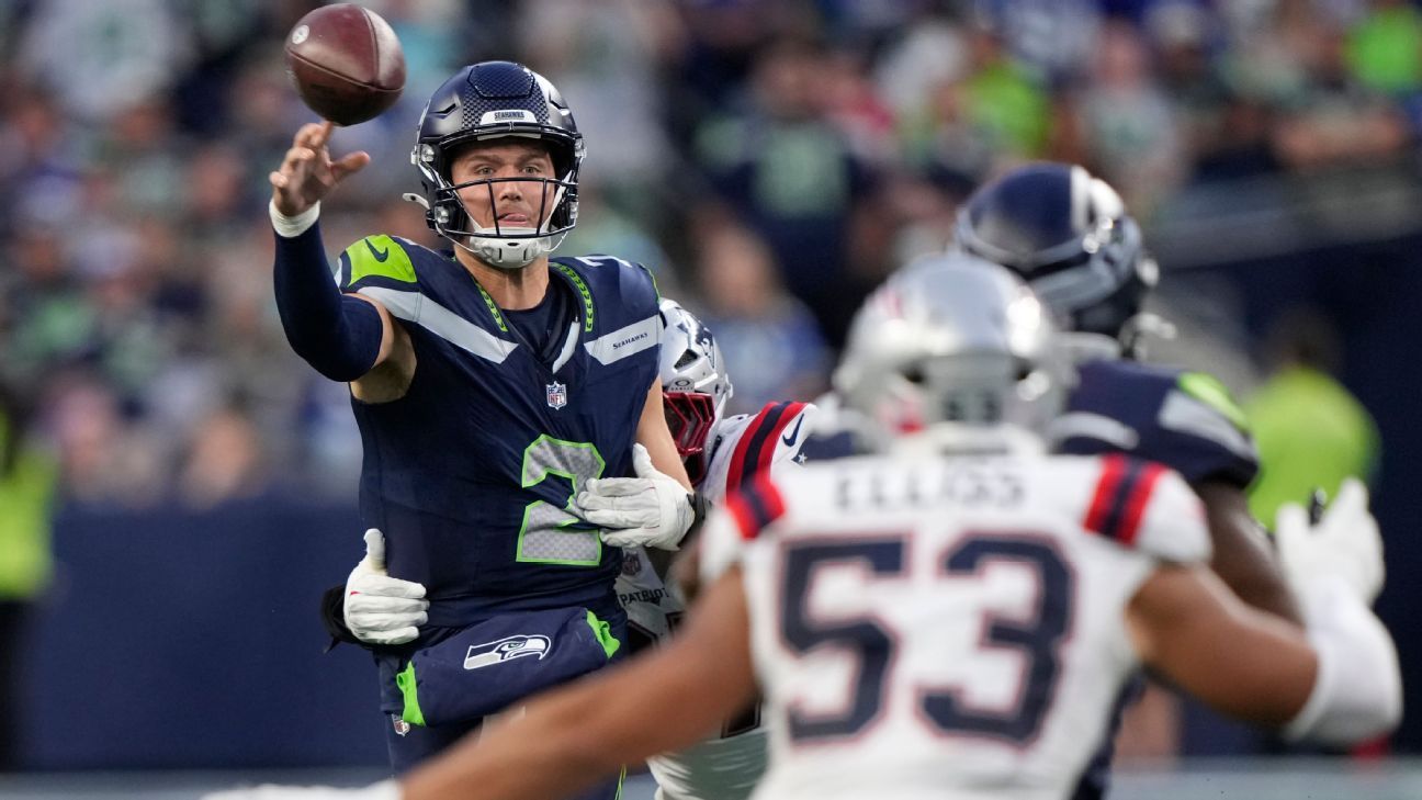 Seattle quarterback throws a football as Patriots defenders pursue during an NFL game.