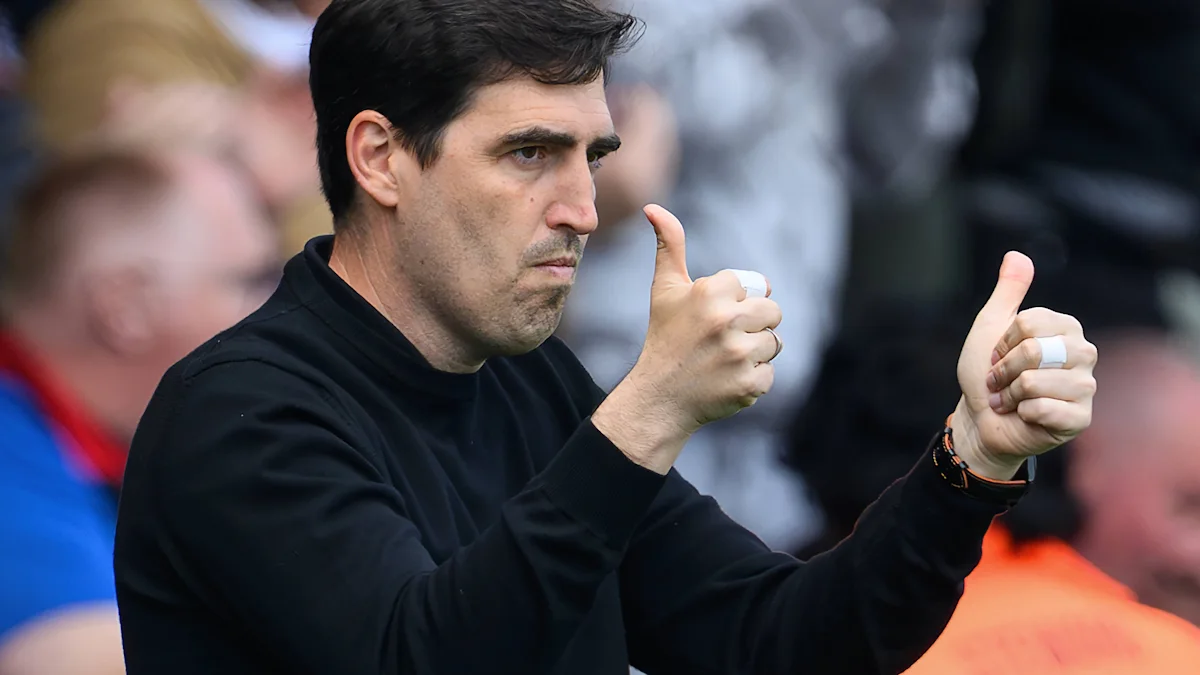 Dark-haired man in a black top gives two thumbs up in front of a blurred crowd.