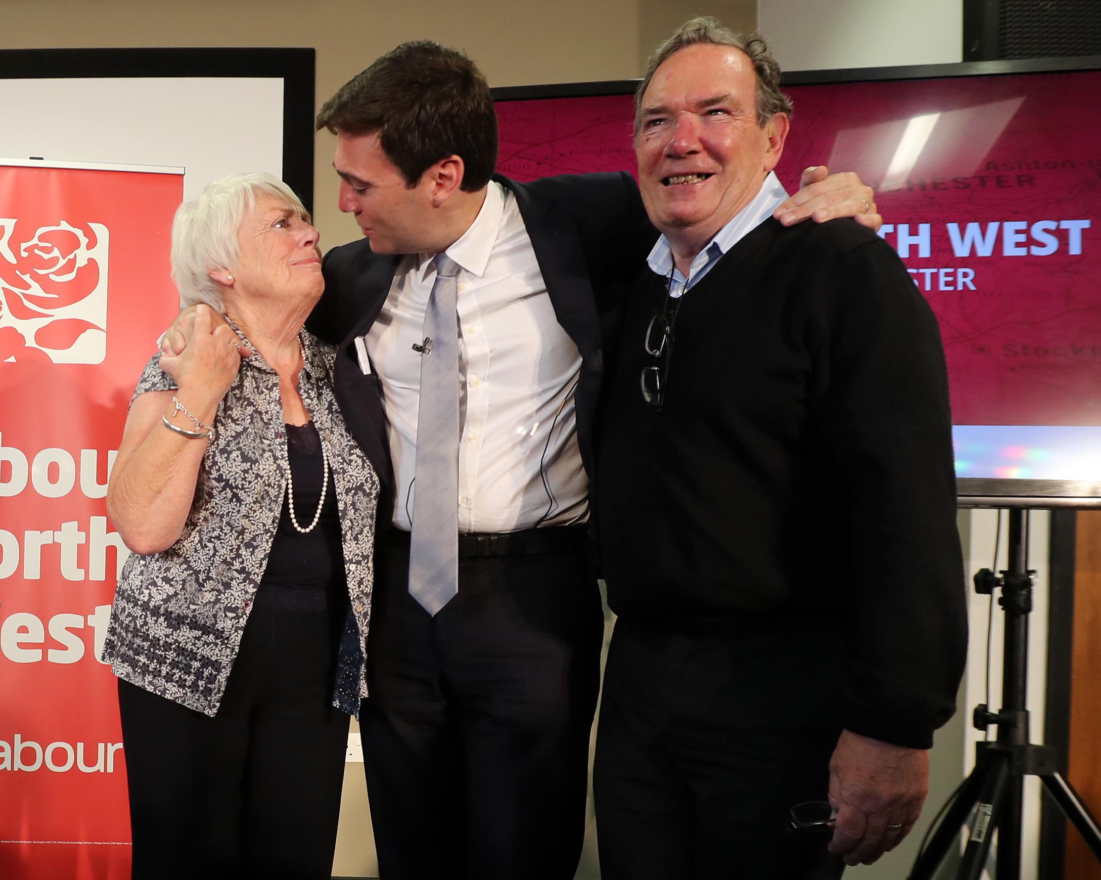 Three people stand together at an indoor event, with a woman and two men embracing.