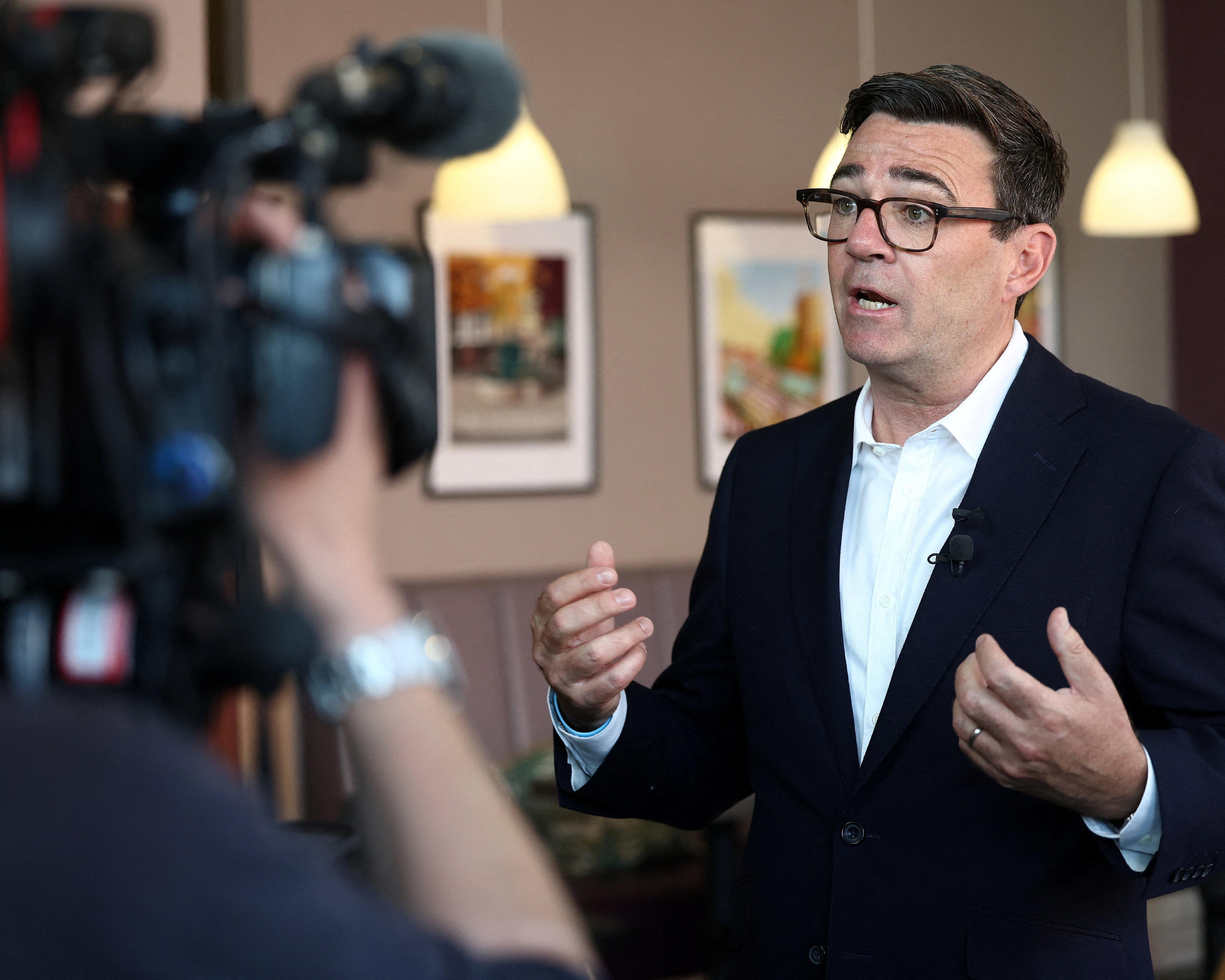 A suited man speaks and gestures during an interview as a television camera films him.