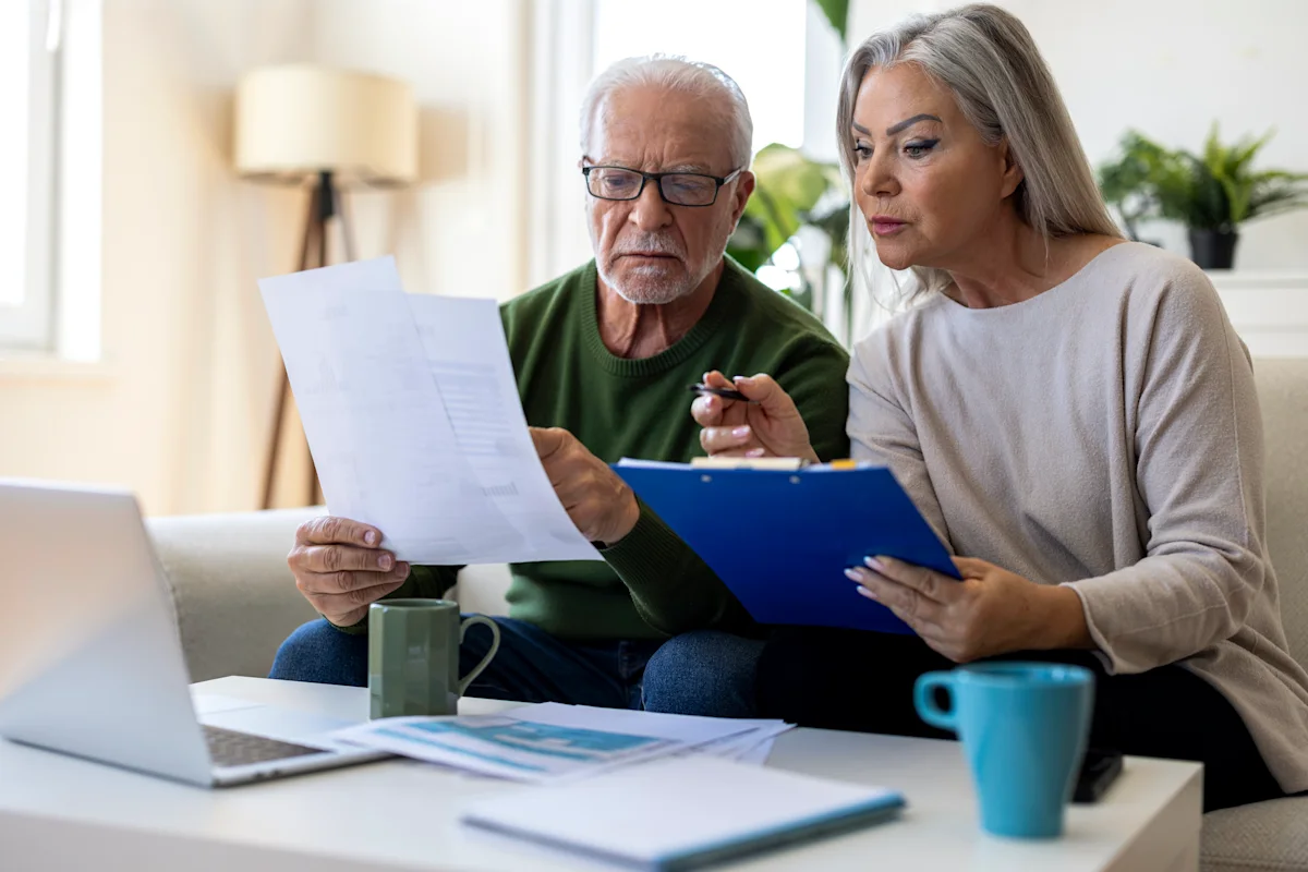 Older couple reviewing financial documents together at home beside a laptop and coffee mugs