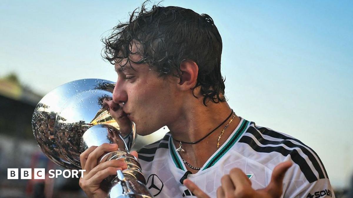 Formula One driver kisses a silver trophy while wearing a black-and-white racing shirt