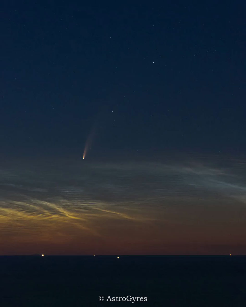 Faint comet with a glowing tail rises above a dark sea beneath a starry night sky.