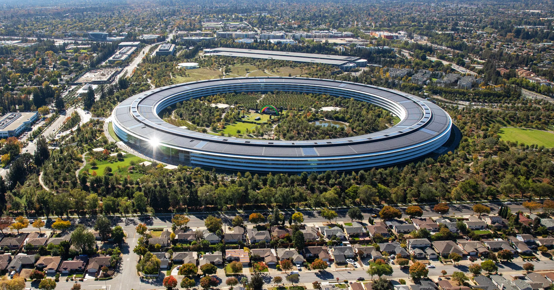 Aerial view of Apple’s circular headquarters surrounded by landscaped grounds, roads, and residential neighborhoods.