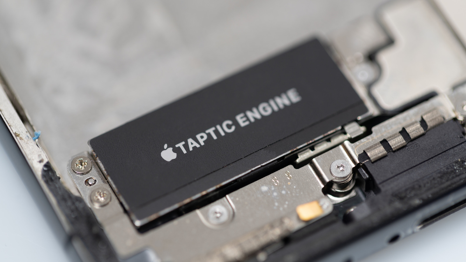 Close-up of an Apple Taptic Engine component inside an opened device, with screws and metal brackets visible.
